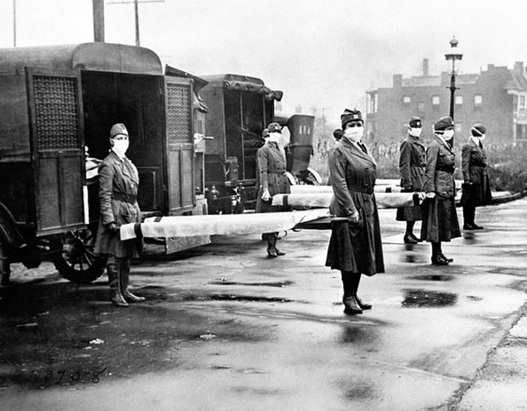 El Cuerpo de Red Cross Motor Corps de St Luis de servicio con mujeres enmascaradas sosteniendo camillas en la parte trasera de las ambulancias durante la epidemia mundial de gripe española, St Luis, Missouri, octubre de 1918. Foto de Underwood Archives/Getty Images.
